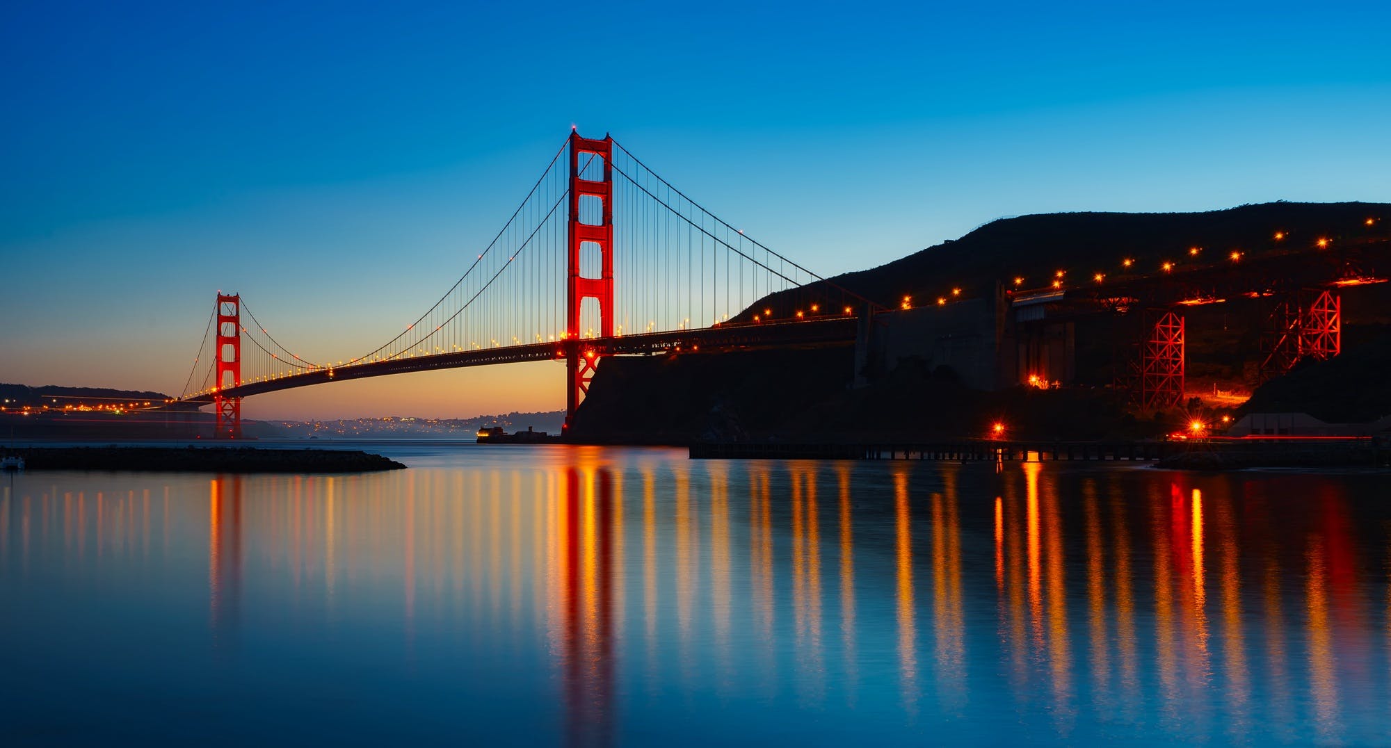 Twilight hues cast a serene glow on the Golden Gate Bridge, with its iconic towers reflecting in the tranquil waters below, epitomizing California's tourism appeal.