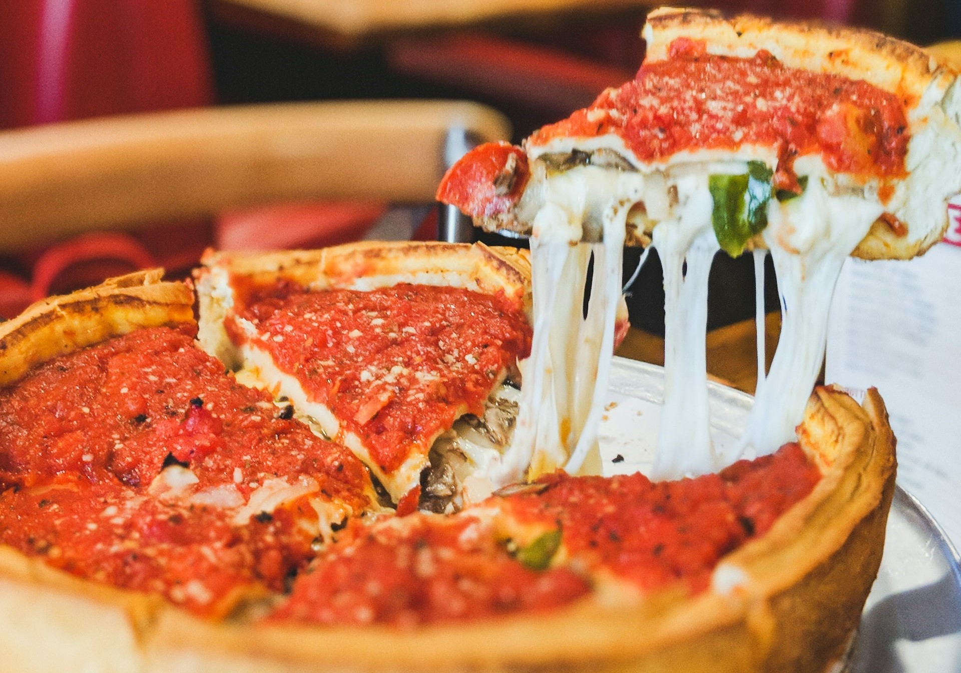 Melty cheese stretching from a freshly lifted slice of deep-dish pizza, highlighting the rich layers of tomato sauce and toppings characteristic of Illinois.