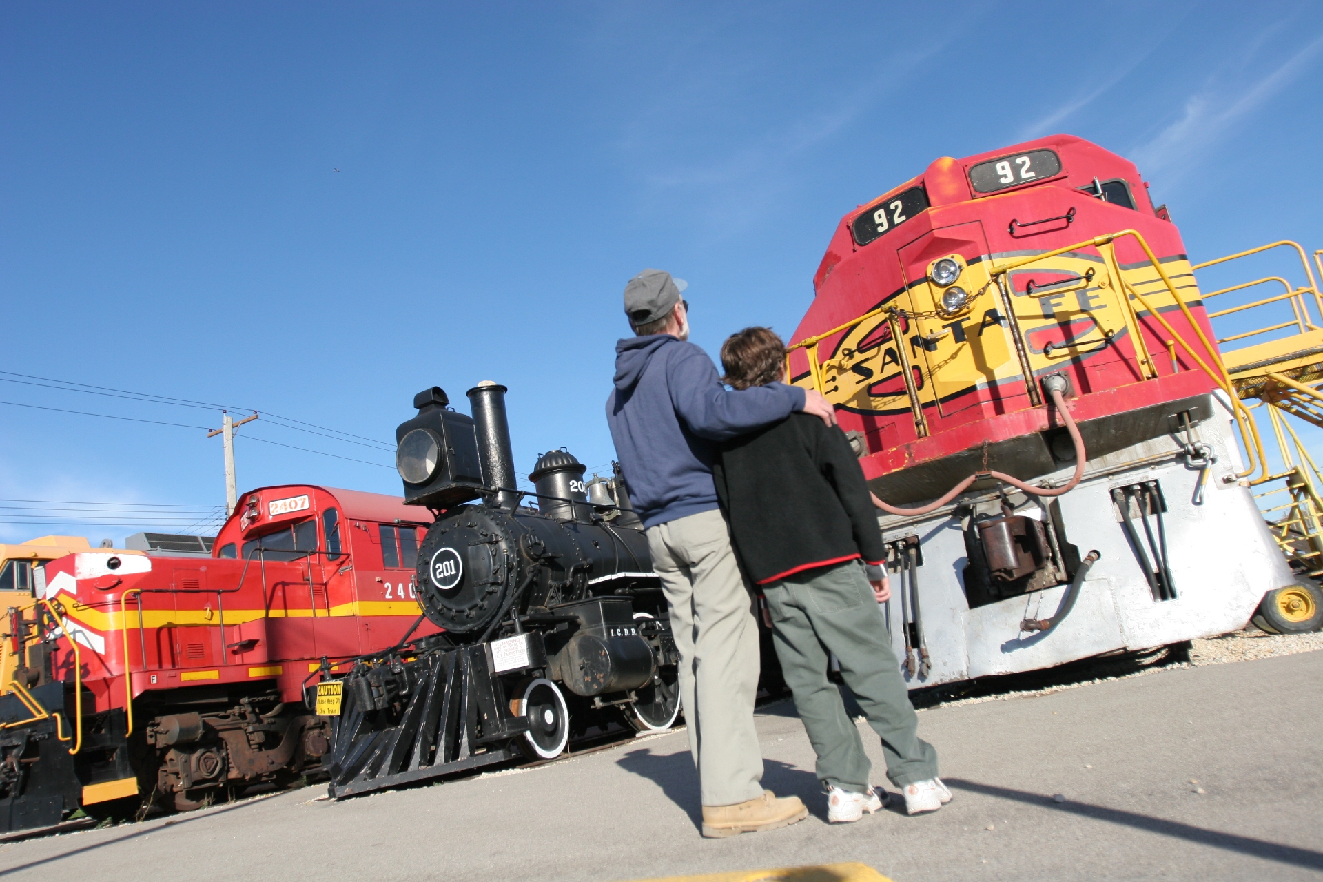 Two people standing close and observing vintage and modern locomotives in Illinois on a sunny day.
