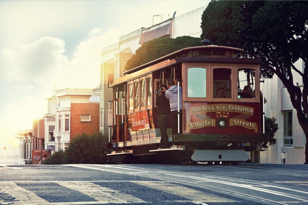 An iconic cable car ascends a steep street in san francisco on a sunlit day, carrying passengers enjoying the ride.