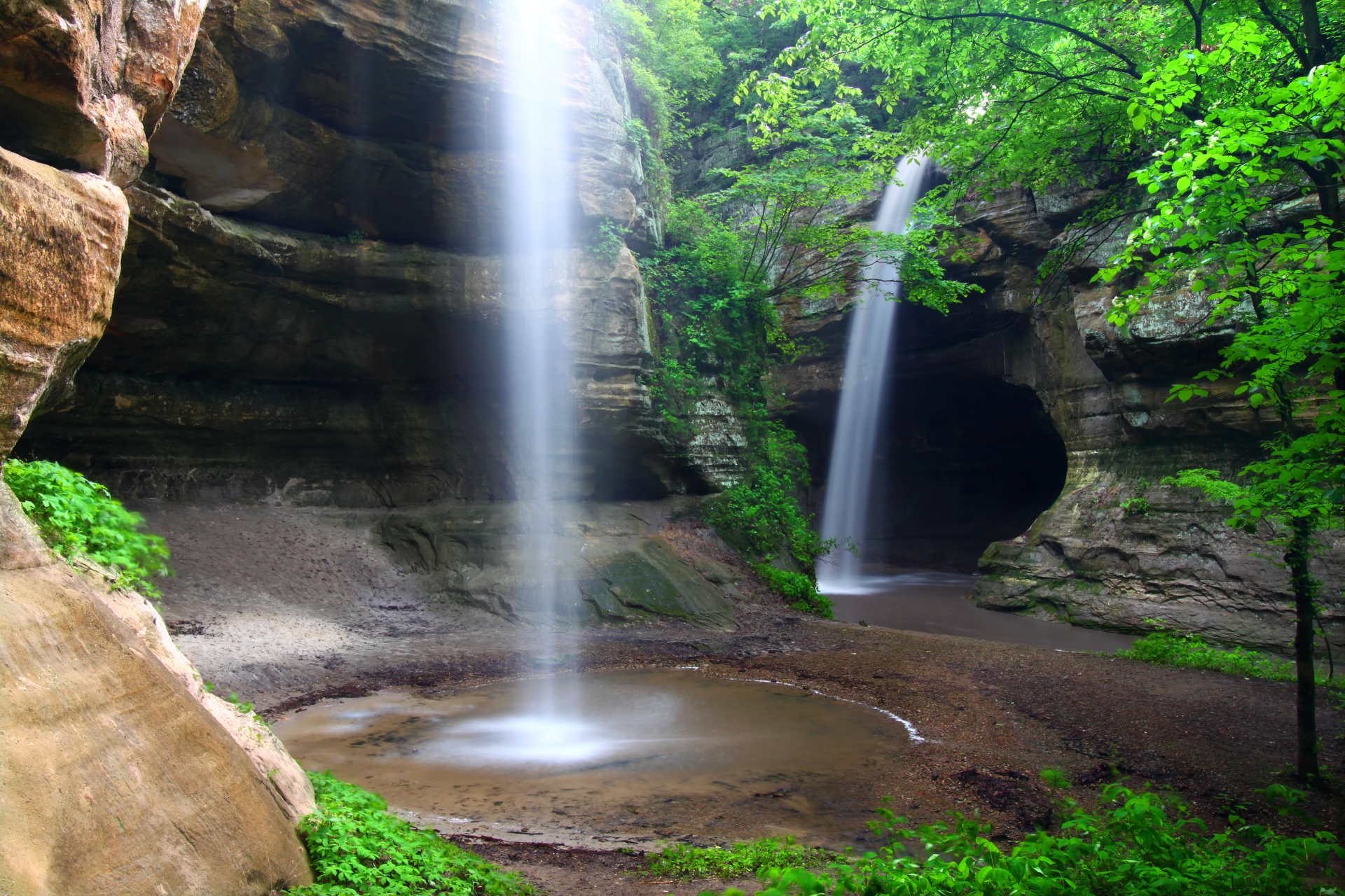A serene waterfall cascades into a tranquil pool surrounded by lush greenery and weathered rock formations in Illinois, creating a picturesque natural oasis.