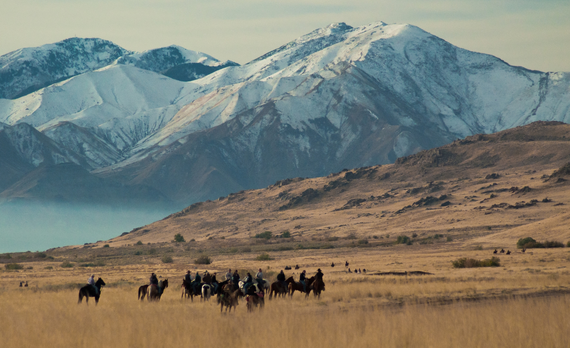 A group of riders journeying across a grassy plain with majestic snow-capped mountains in the background.
