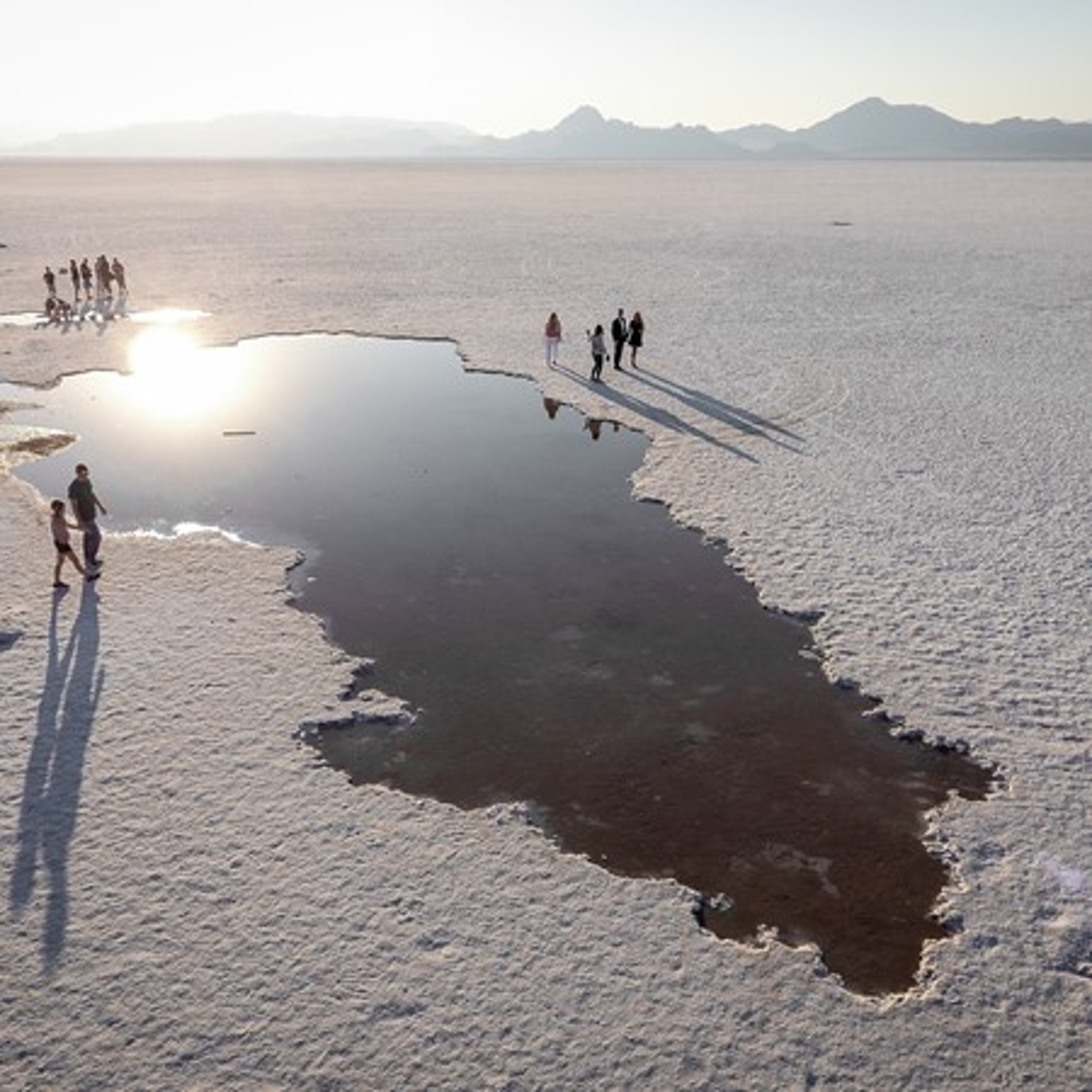 A serene sunset at a vast salt flat, with a group of travelers gathered around a reflective pool of water, creating a tranquil and picturesque scene.