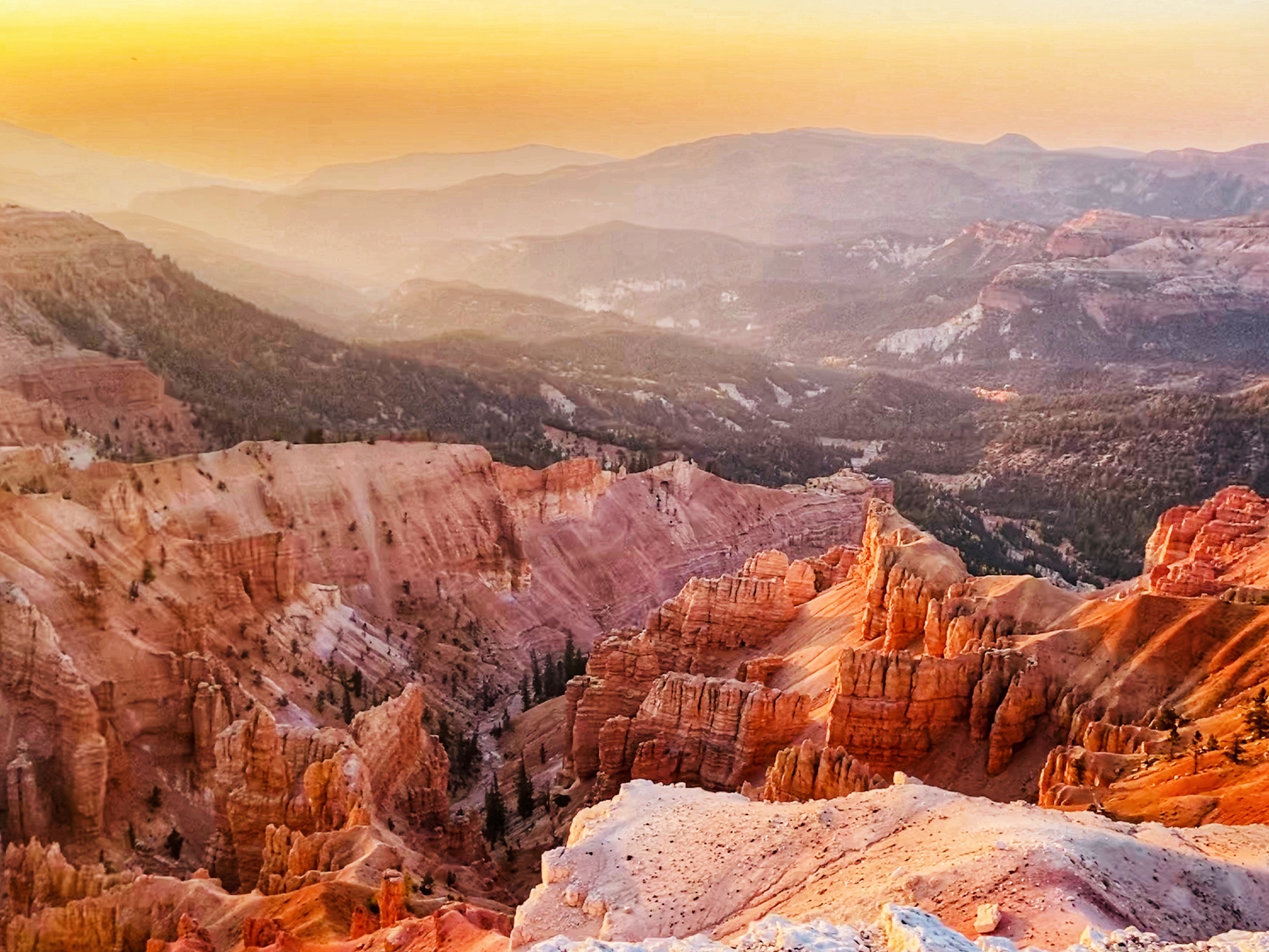 Sunset glow bathes the rugged landscape of a canyon, casting a warm, golden hue over its stratified rock formations and the expansive view beyond.