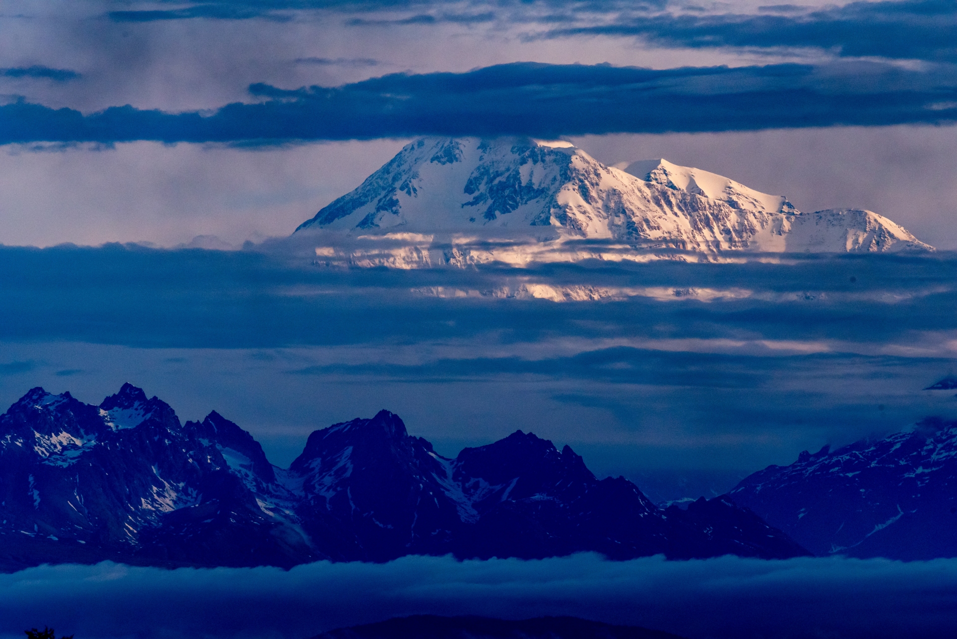 Majestic snow-capped peaks piercing through a blanket of clouds under a twilight sky.