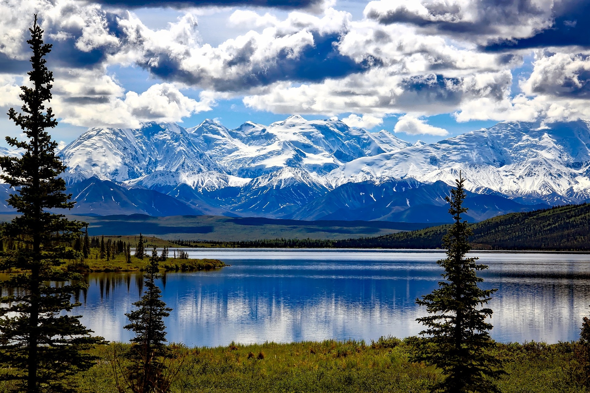Majestic snow-capped mountains overlooking a tranquil lake, with lush greenery framing the serene landscape.