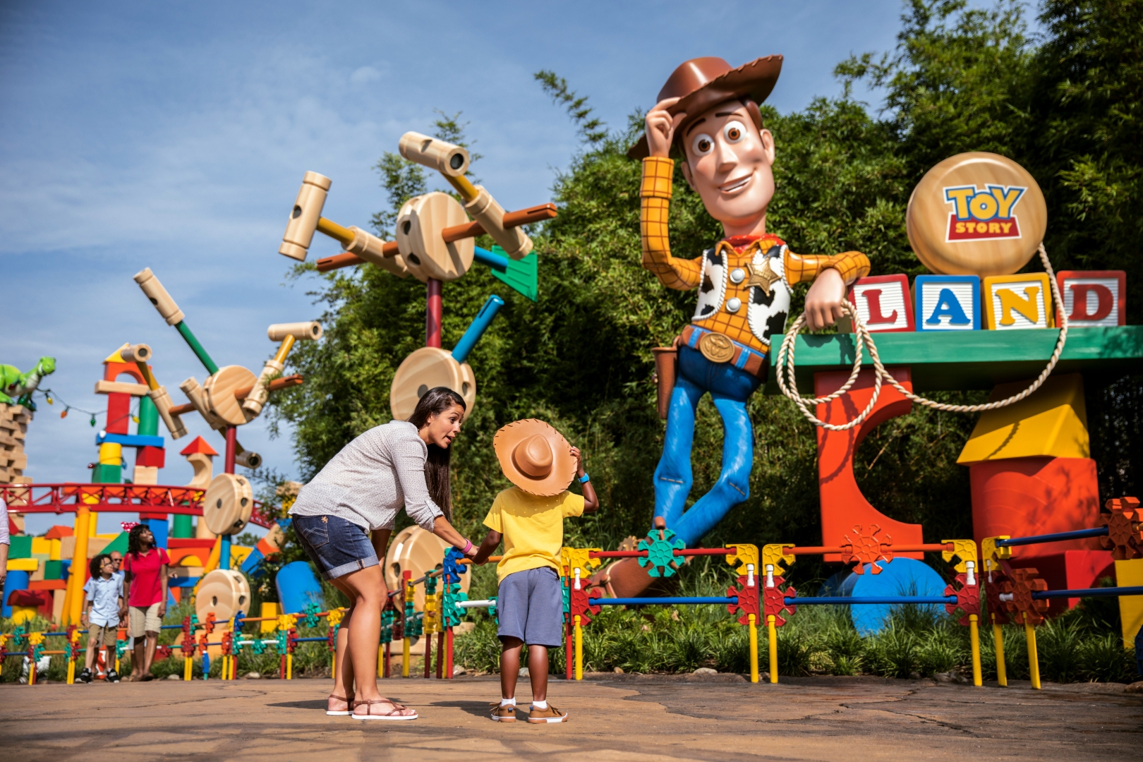 A joyful family moment in toy story land as a child aims to lasso like a cowboy under the watchful eye of an oversized woody figure.