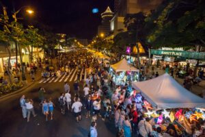 Bustling evening street market alive with shoppers and colorful stalls under the warm glow of city lights.
