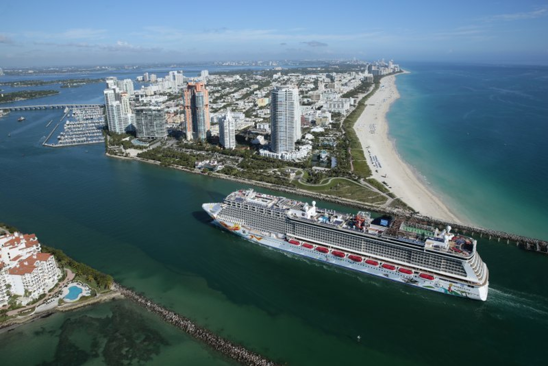 Aerial view of a large cruise ship departing a tropical coastal city with high-rise buildings and expansive beaches, embarking on one of its scheduled voyages.