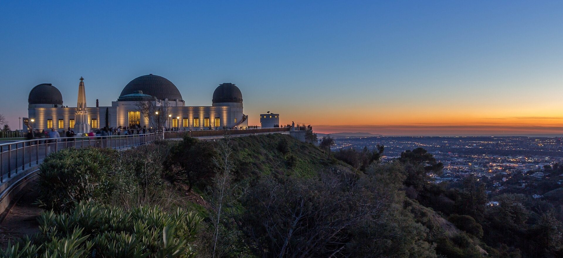 Twilight descends over a scenic observatory in Los Angeles, as visitors enjoy panoramic views of the city stretched out beneath a gradient sunset sky.