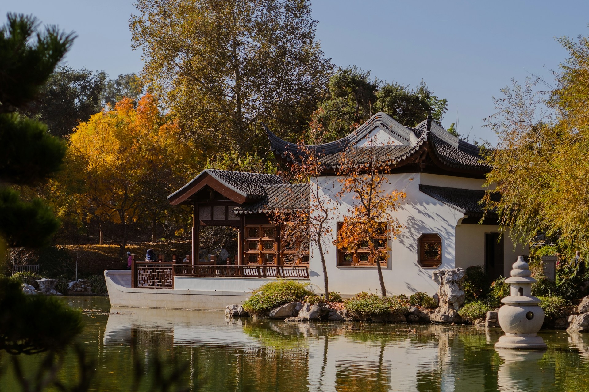Traditional Chinese architecture nestled among autumn foliage beside a tranquil pond in Los Angeles.