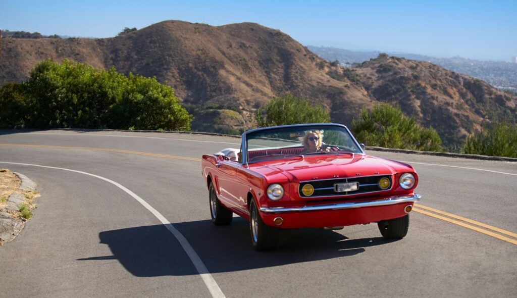 A sunny day road trip cruise along a winding road with a classic red convertible.