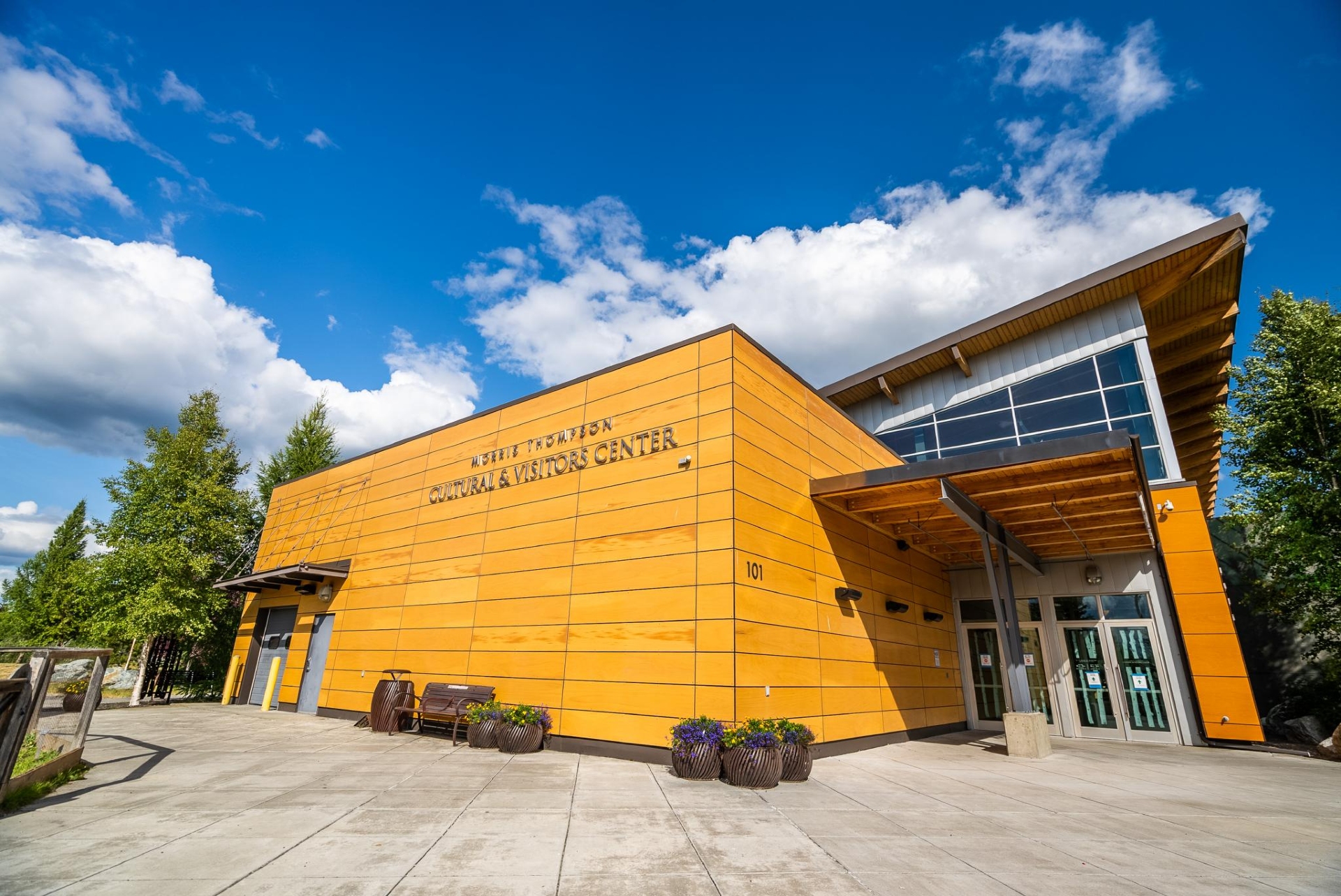 A modern visitor center with a vibrant orange facade under a sunny sky with clouds, showcasing a welcoming entrance and an eco-friendly design.