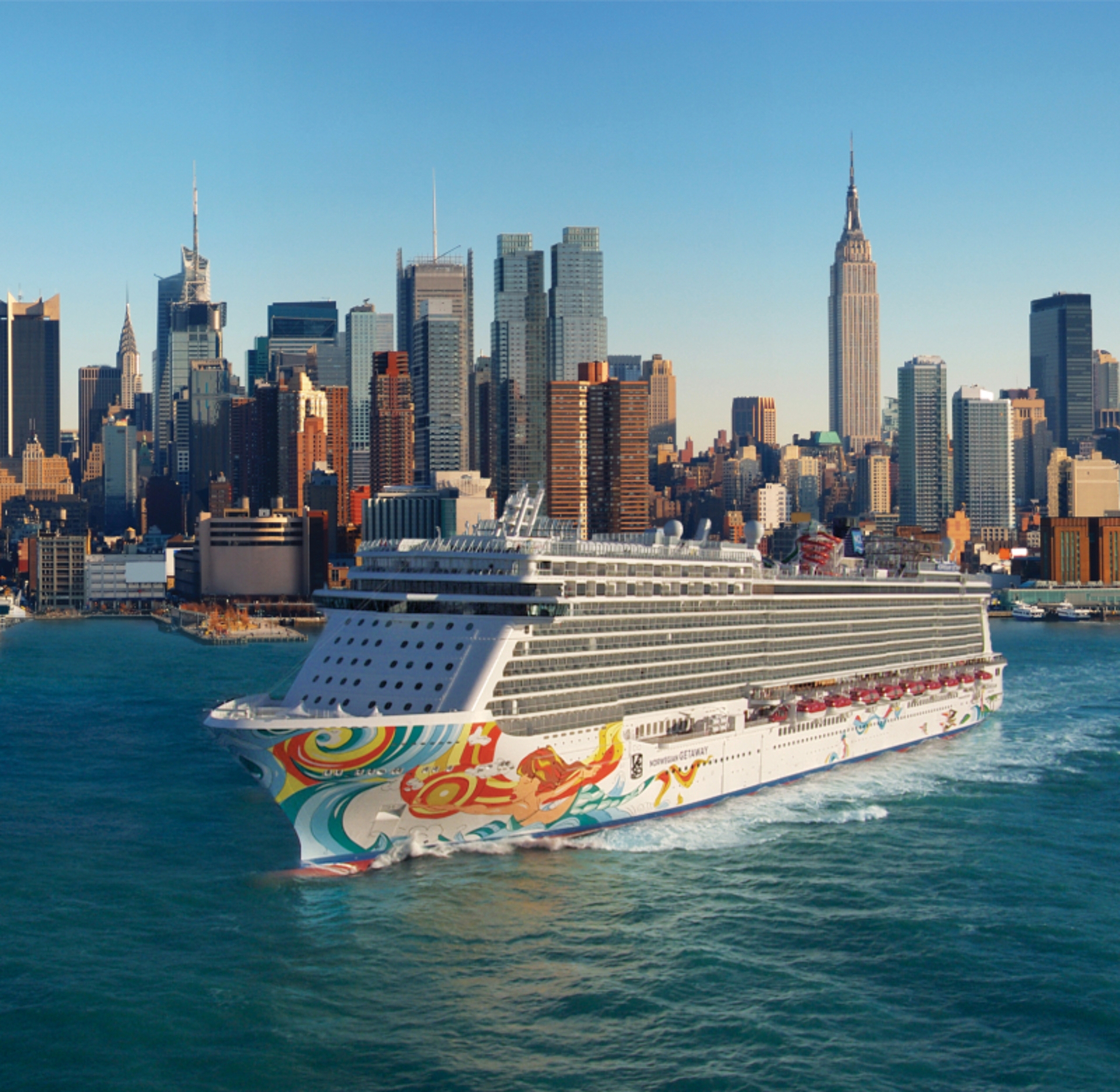 A vibrant cruise ship makes its way in front of a striking New York City skyline, with the iconic Empire State Building standing tall in the background, offering an unforgettable cruising voyage.