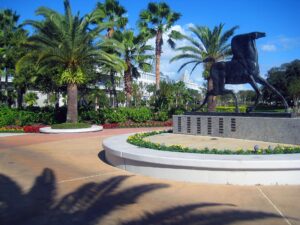 A majestic horse statue surrounded by vibrant flowers and palm trees under a clear blue sky.