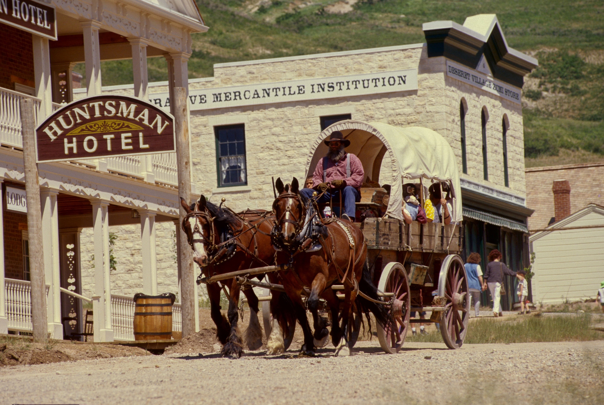 A horse-drawn stagecoach carrying passengers rolls through a historic town reminiscent of the old west.