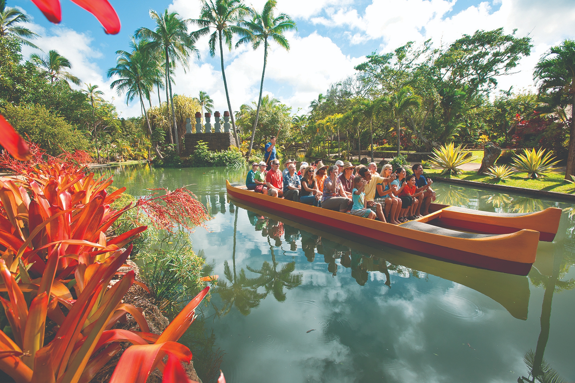 A group of tourists enjoying a guided boat tour on a tranquil tropical waterway surrounded by lush vegetation and vibrant flowers.