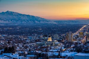 Twilight over a snowy cityscape: a serene view of a city illuminated by the warm glow of sunset, with snow-capped mountains standing vigil in the background.