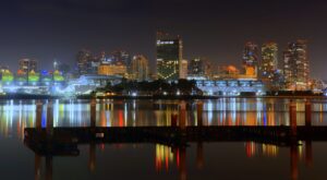 A serene night cityscape reflecting on the calm waters, with colorful illuminated buildings creating a vibrant urban glow.
