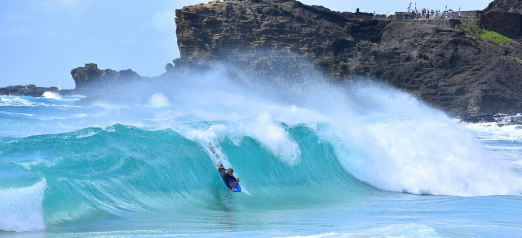 A bodyboarder riding a powerful wave with a rocky cliff in the background.