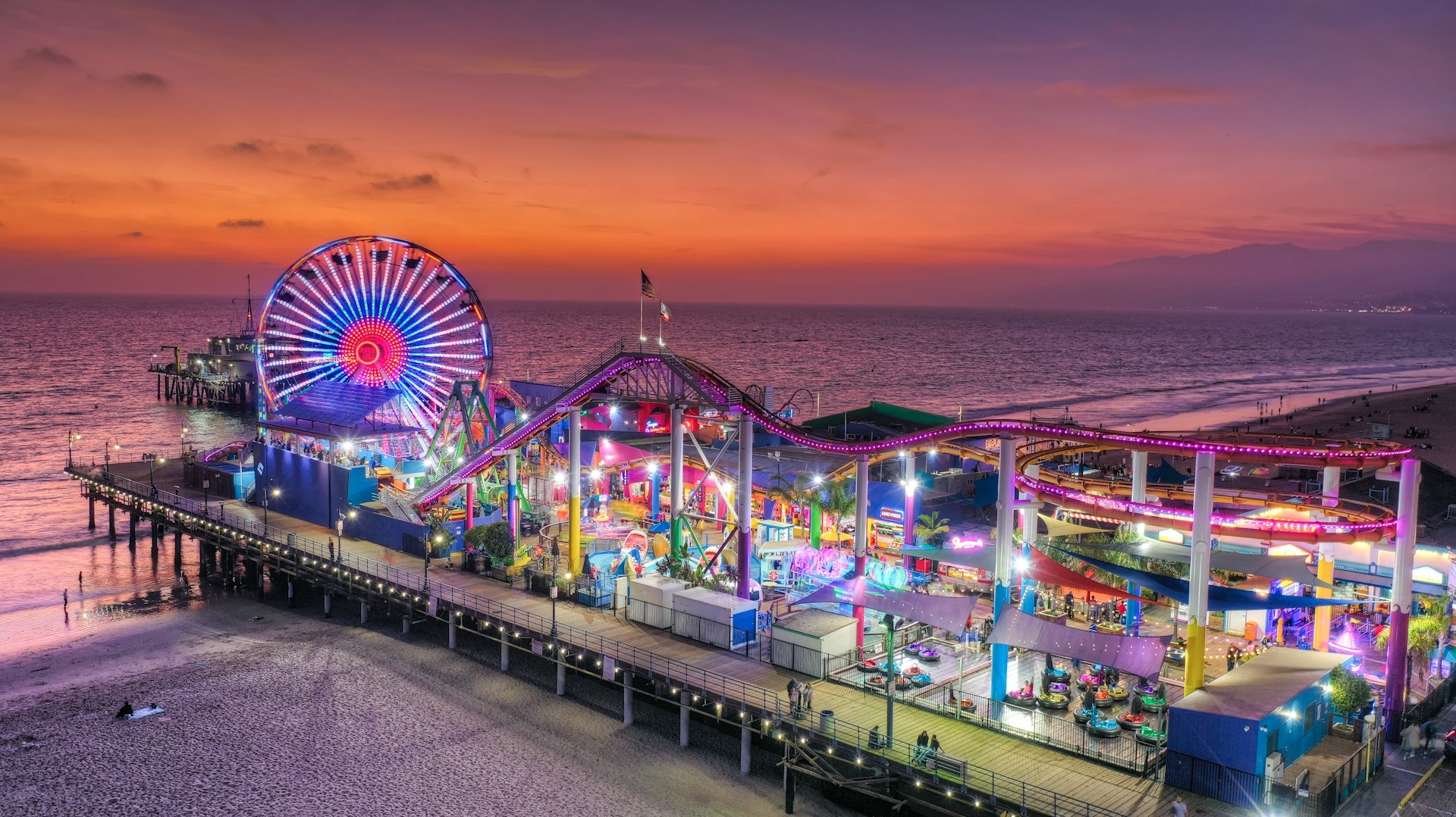 A vibrant evening at the Los Angeles pier, with a ferris wheel illuminating the twilight sky and the amusement park bustling with life.