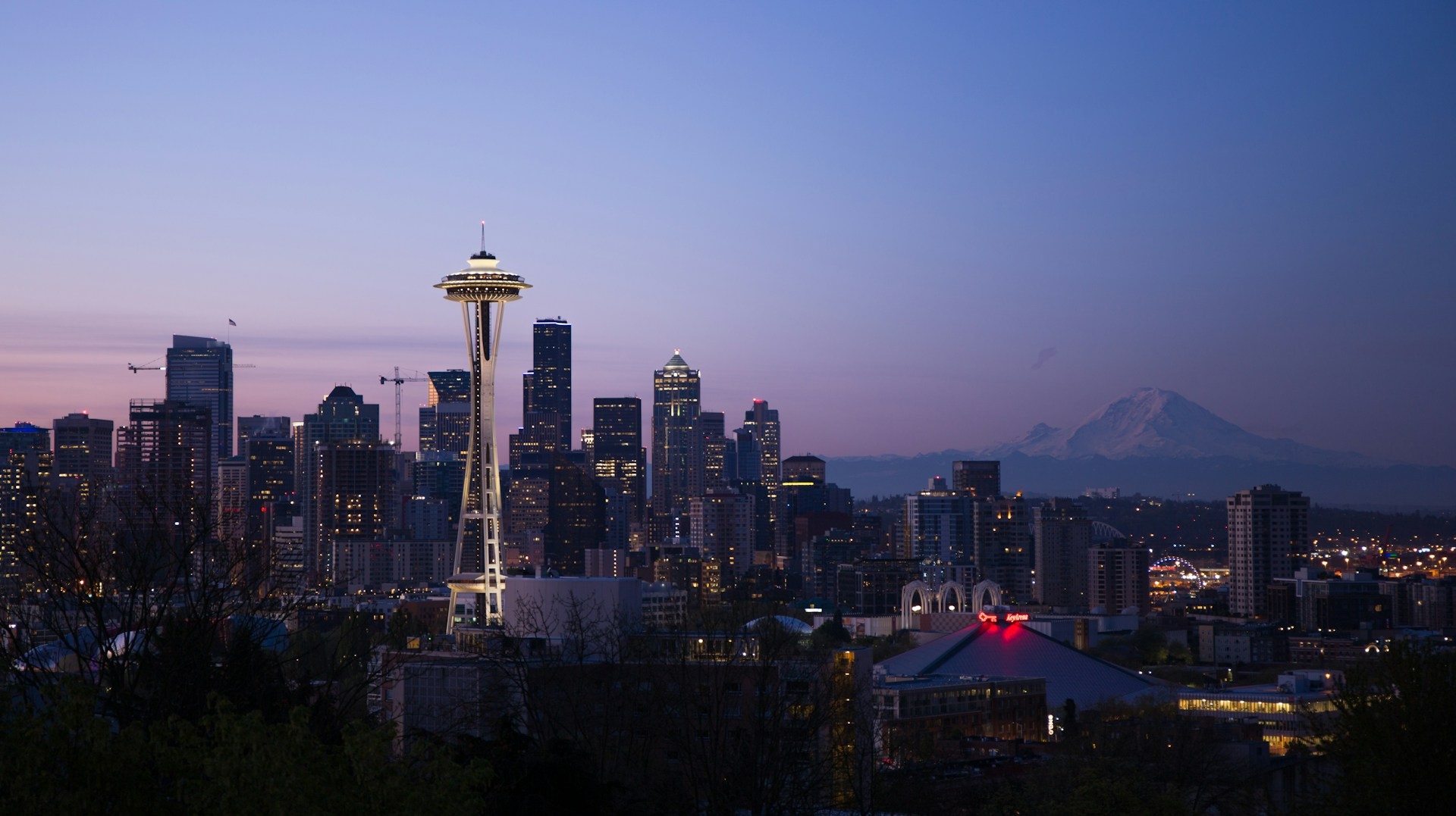 Twilight descends on the seattle skyline, with the iconic space needle standing tall against the backdrop of a serene mount rainier.