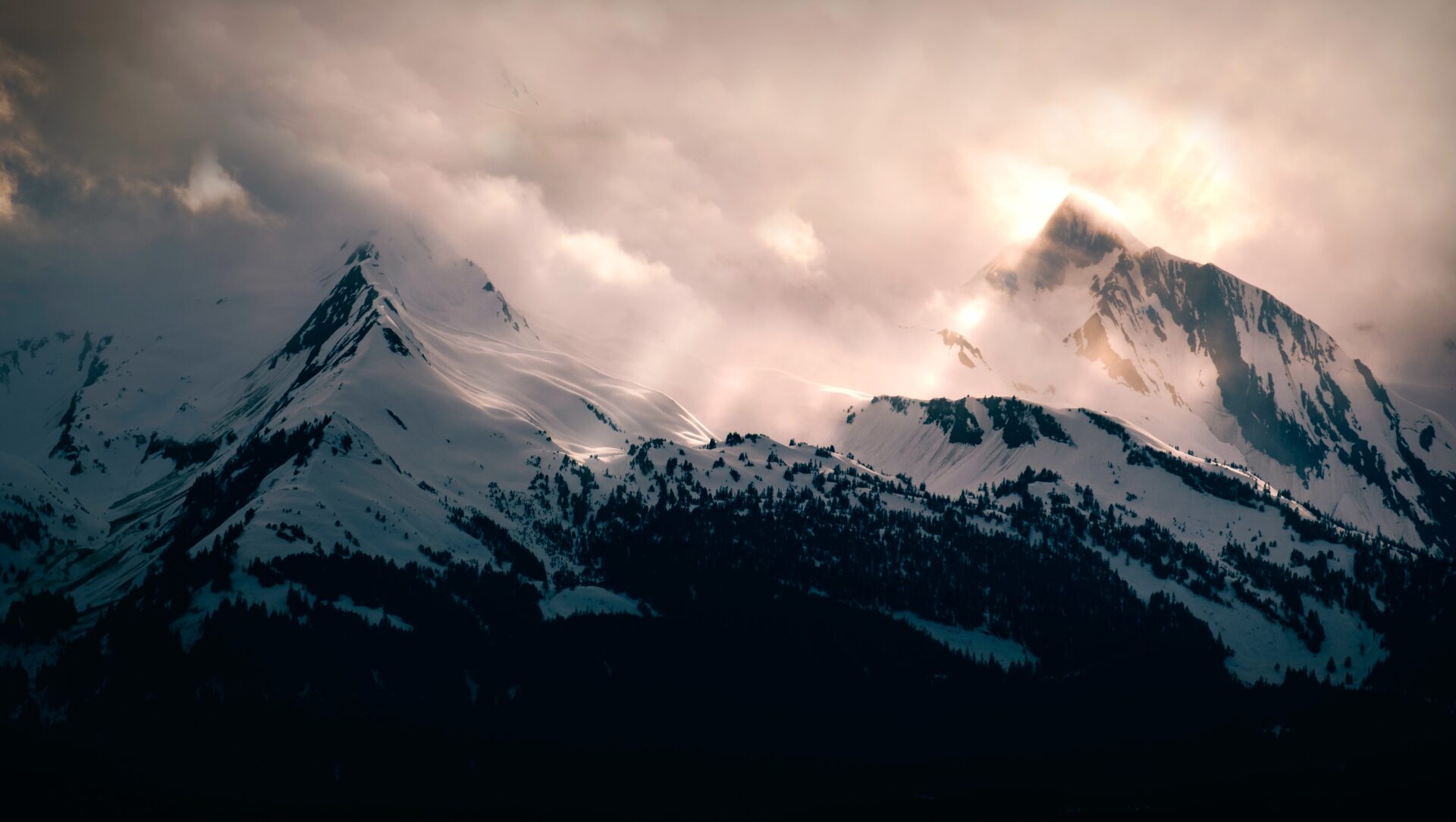 Majestic snow-capped mountains bathed in the ethereal glow of sunlight piercing through dramatic clouds.