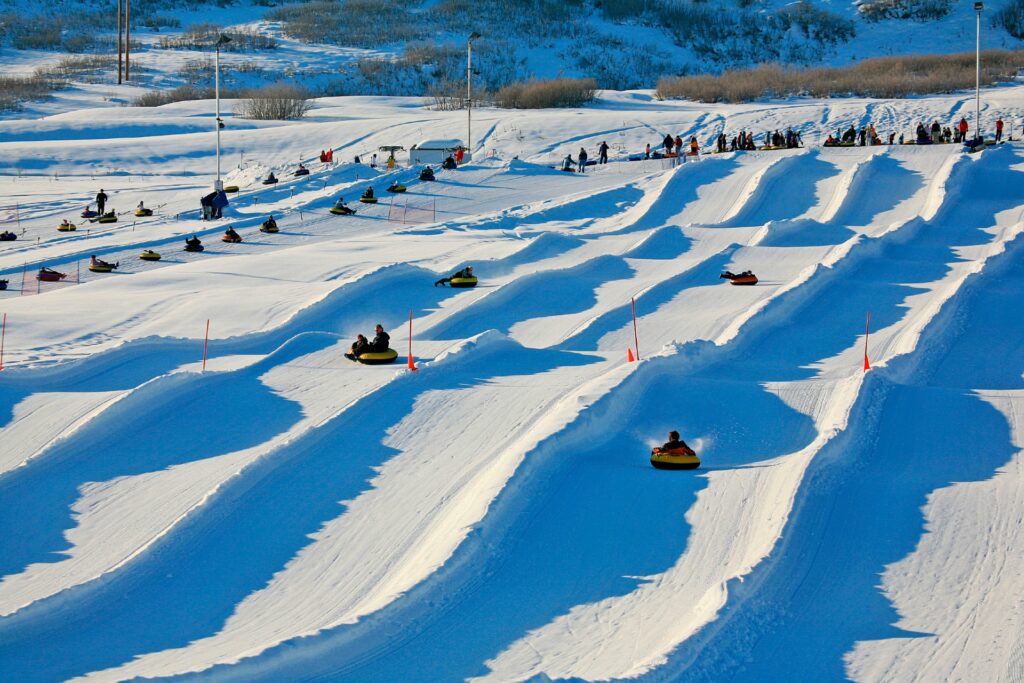 A group of people enjoying a sunny day of snow tubing down a series of snowy lanes on a winter hillside.