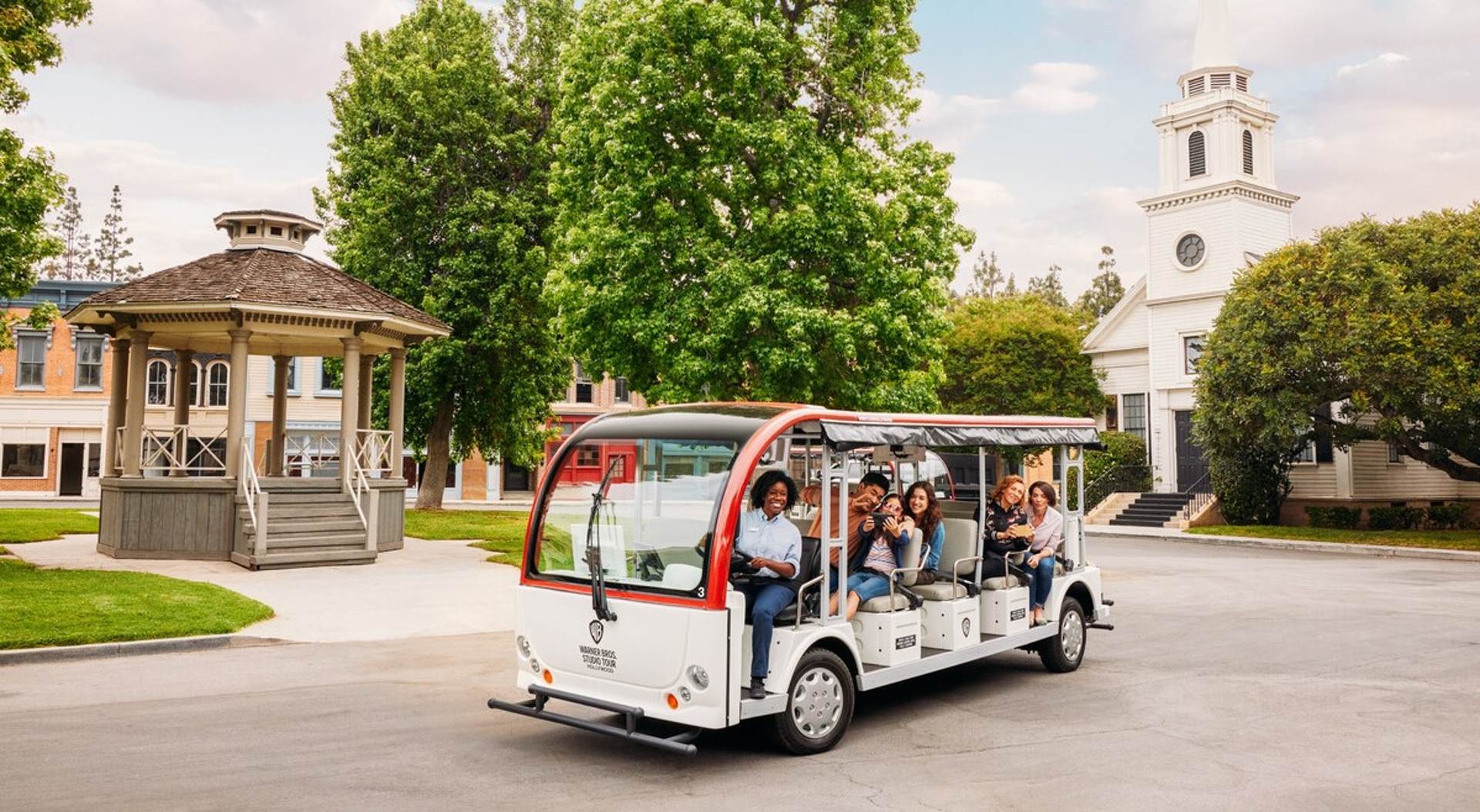 Group of happy people enjoying a tour on an open-air shuttle through a scenic park with classic architecture in Los Angeles.