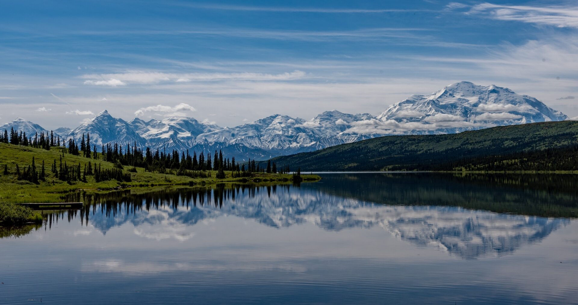 A serene mountain lake reflecting snow-capped peaks under a blue sky dotted with clouds.