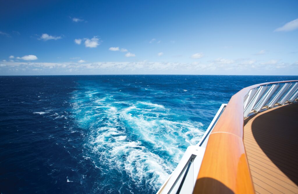 Endless blue: a serene view from the deck of a ship, gazing into the vast ocean under a bright, cloud-scattered sky.