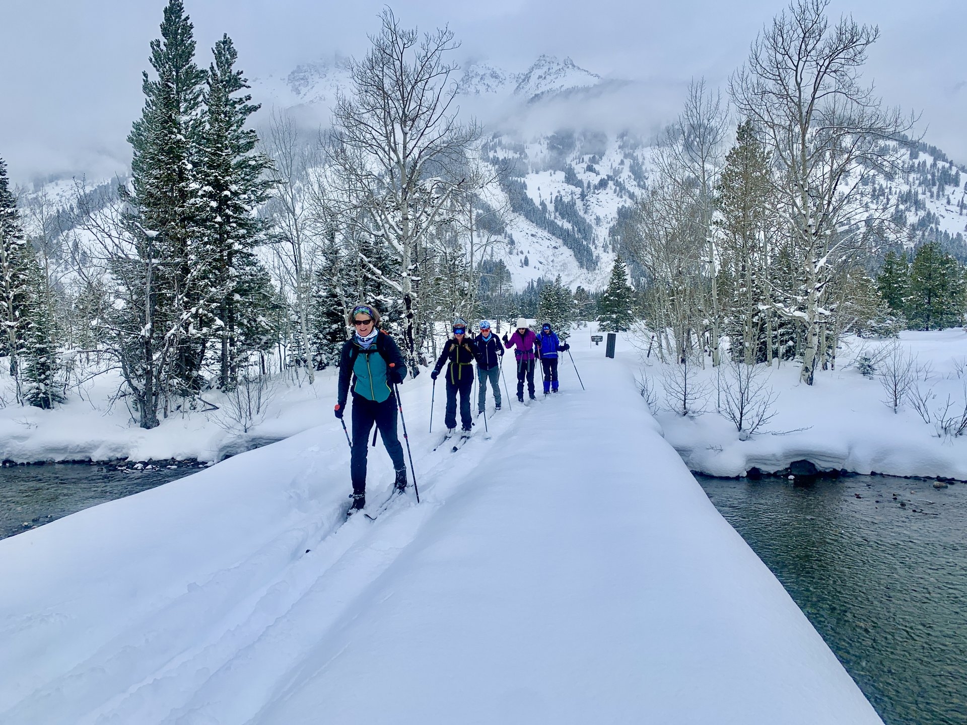Jackson Hole Cross Country Ski crossing the bridge over the river with snow capped mountains in the background