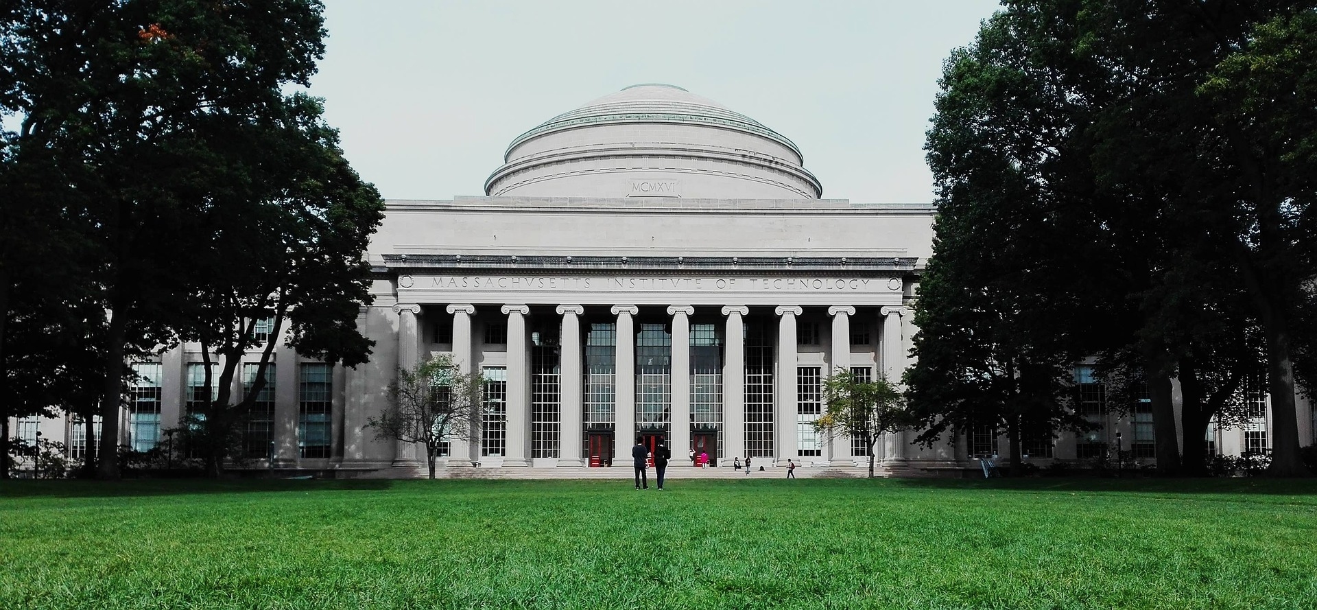 Massachusetts Cambridge University Tech Institute showing the outside view with massive trees either side & green grass in the foreground