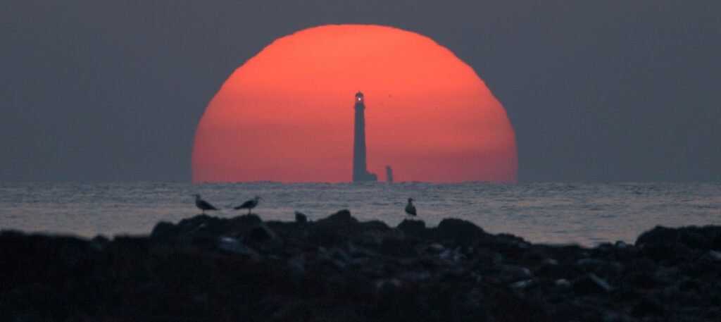 Boon Island sunset Maine stunning image of the sun setting behind the lighthouse tower with birds sitting on the rocks in the foreground