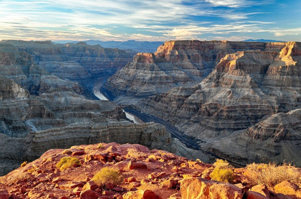 Grand Canyon with sun shining on the foreground rocks while looking below at the Colorado River between the rock formations