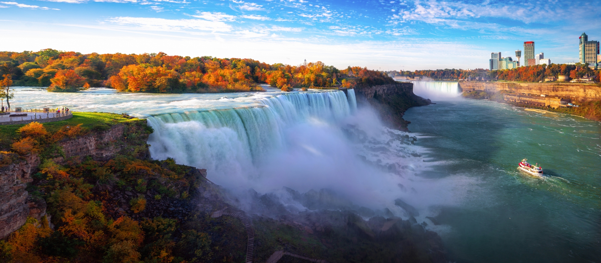 Niagara Falls in Fall season showing the boat of tourists viewing from below and people next to the falls above in the fall season