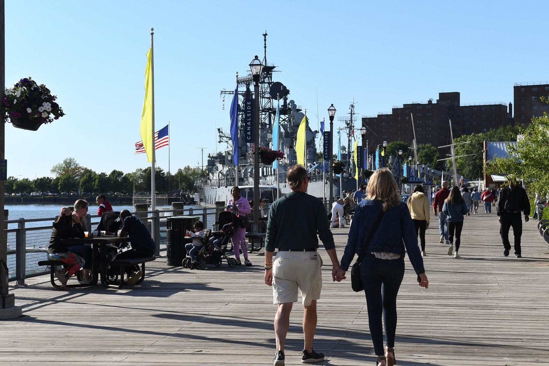 Buffalo Heritage Carousel Canel Side with people walking along the boardwalk with a battleship in the background