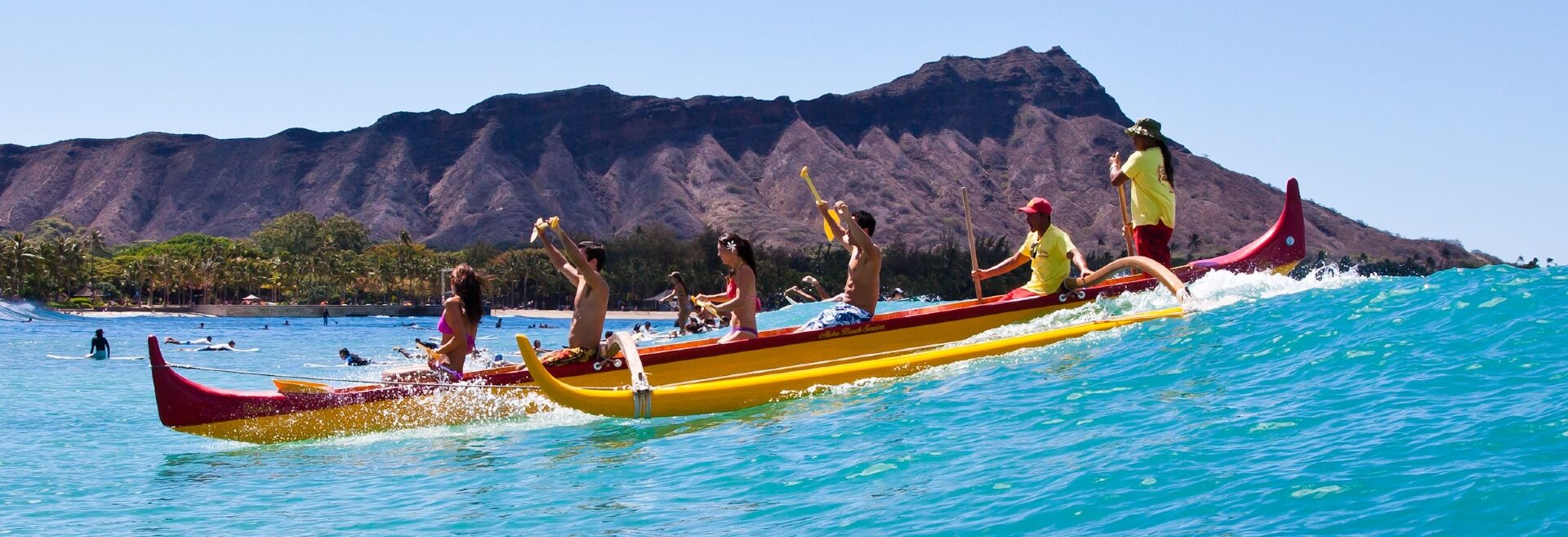 Teamwork at sea: a group of paddlers in a vibrant yellow outrigger canoe glides through turquoise waters with a scenic mountain backdrop.